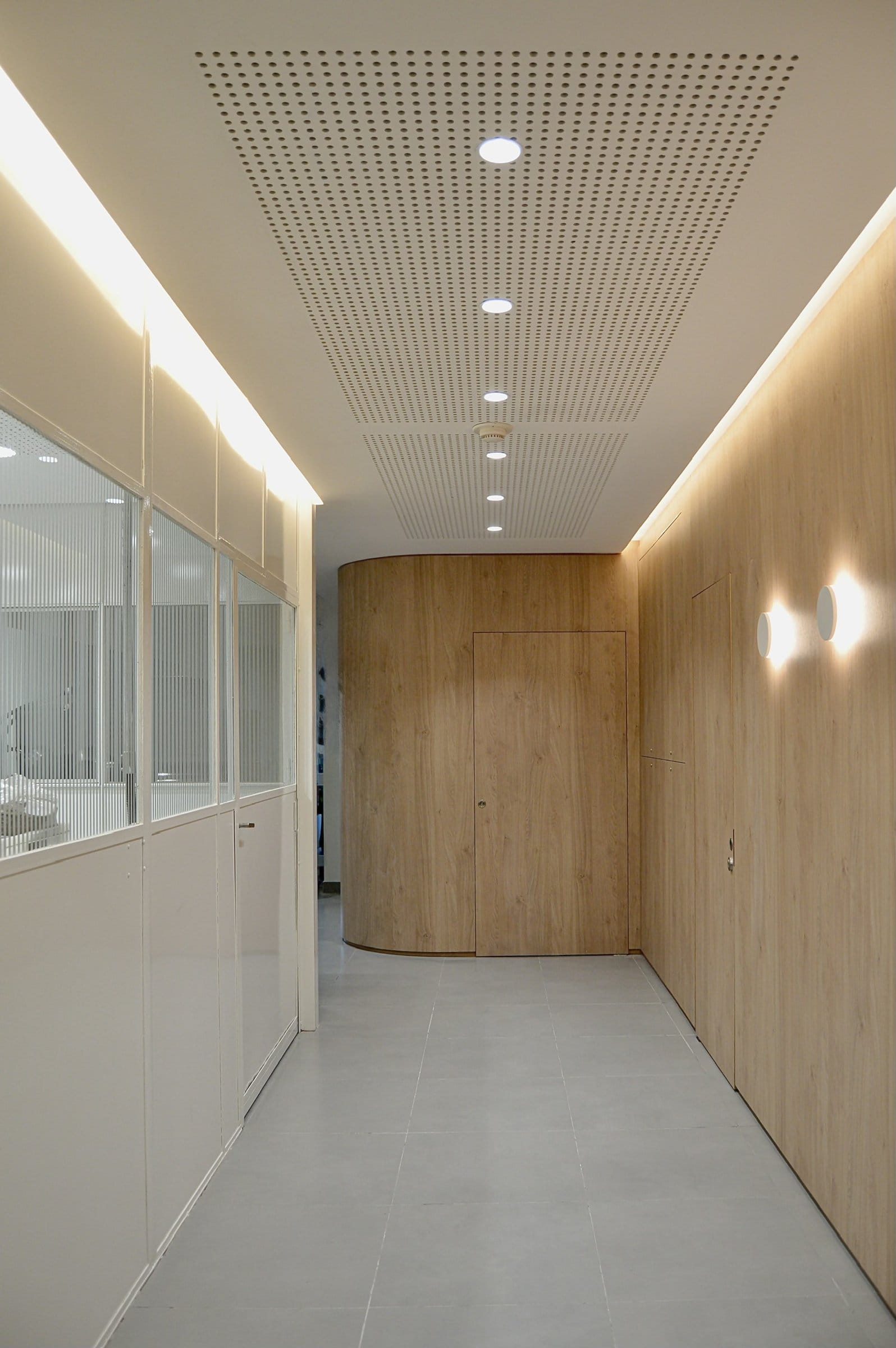 Pasillo con piso de madera, pared de listones y apliques circulares