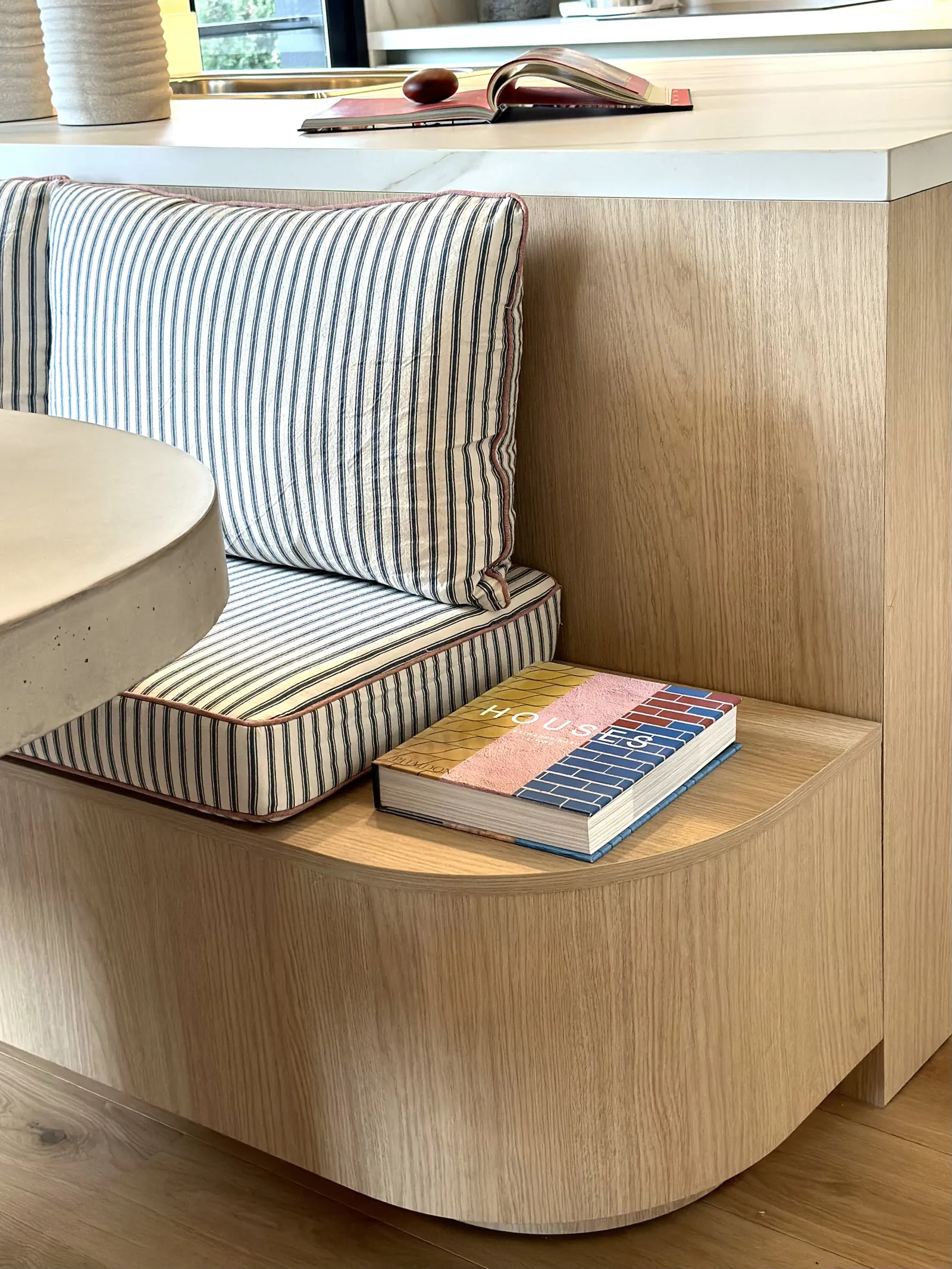 Banco tapizado a rayas junto a una mesa de madera, con libros y una lámpara