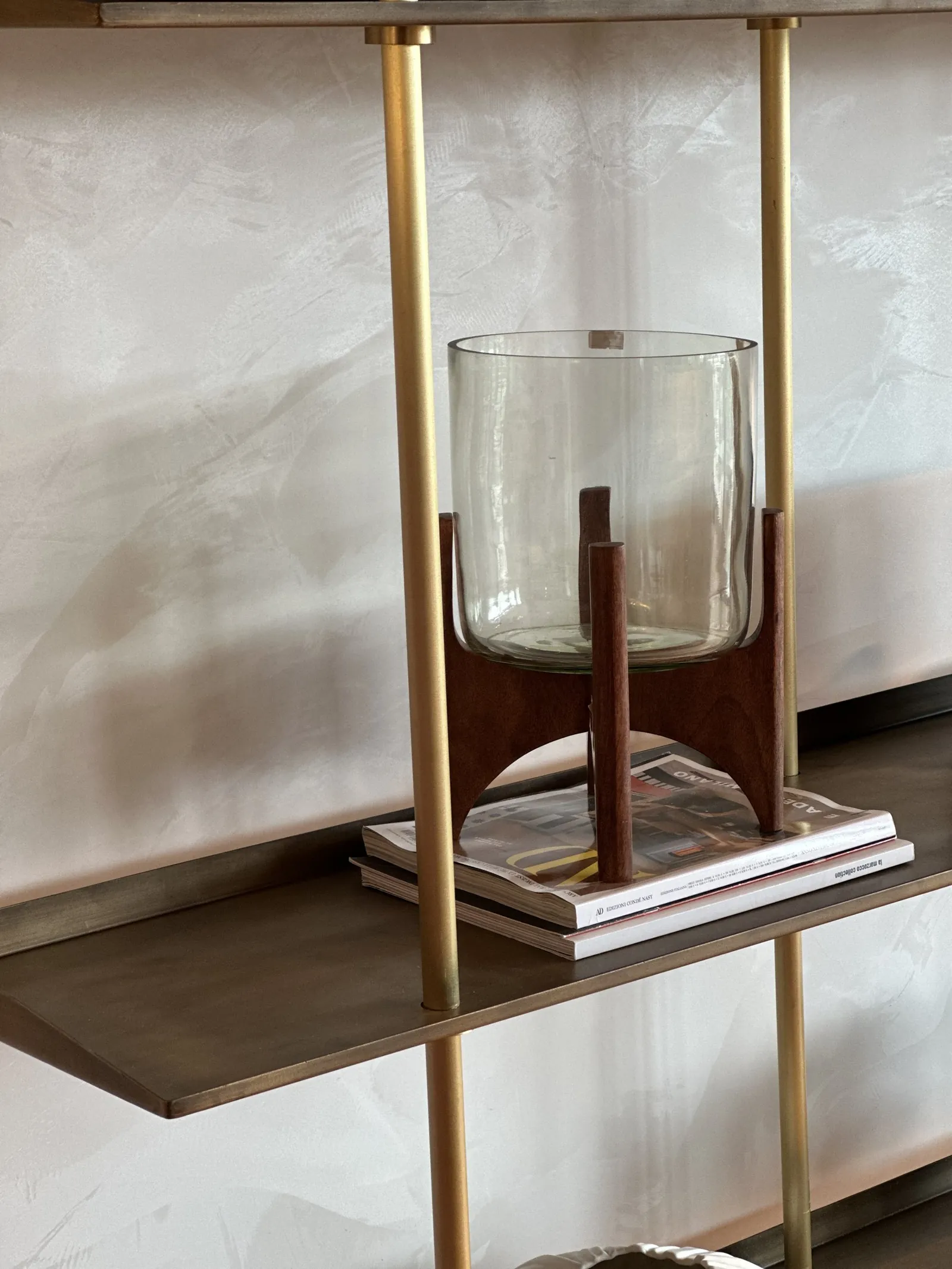 Estantería de vidrio y bronce con un frasco de vidrio sobre un soporte de madera