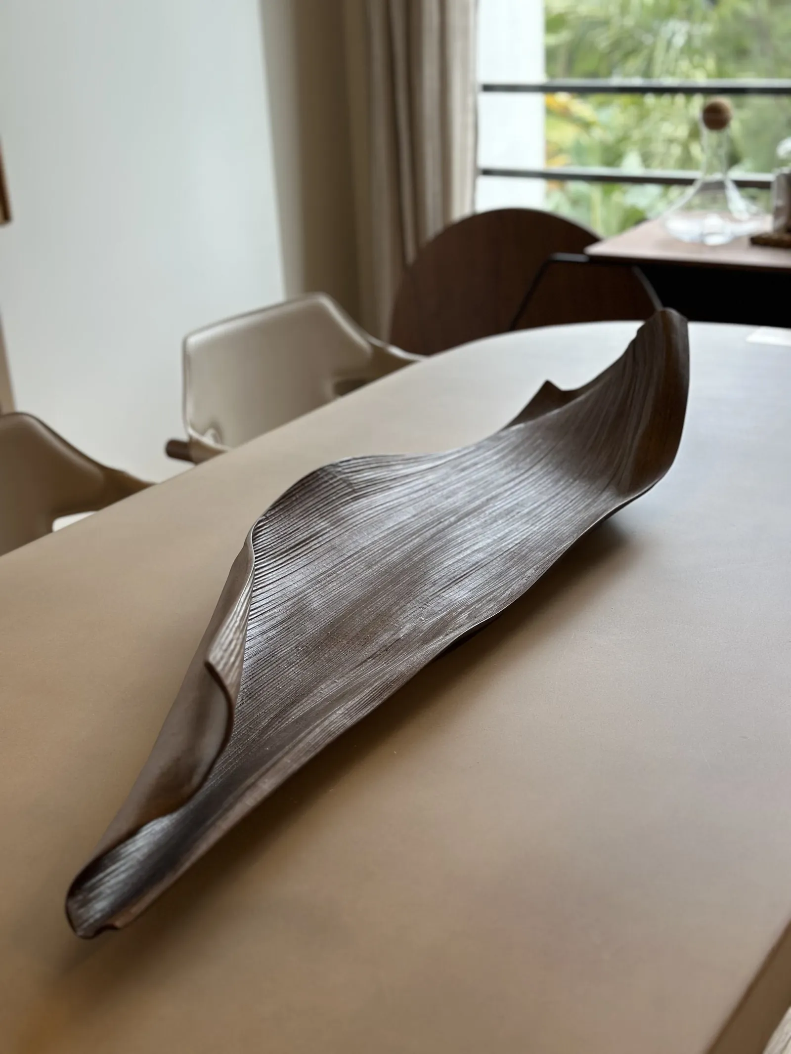 Fuente de madera alargada sobre una mesa, con sillas tapizadas al fondo