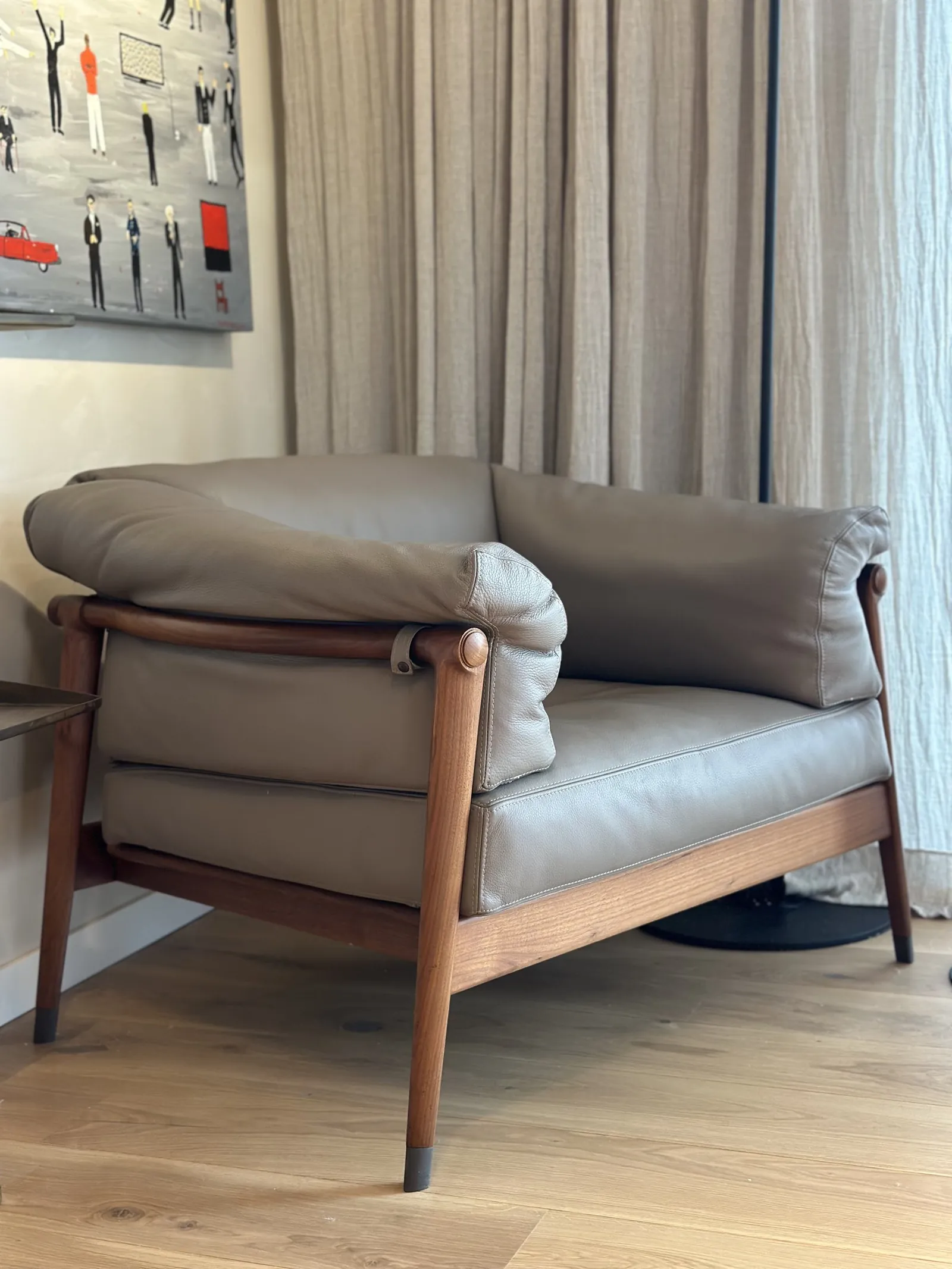 Sillón de cuero con estructura de madera, frente a cortinas