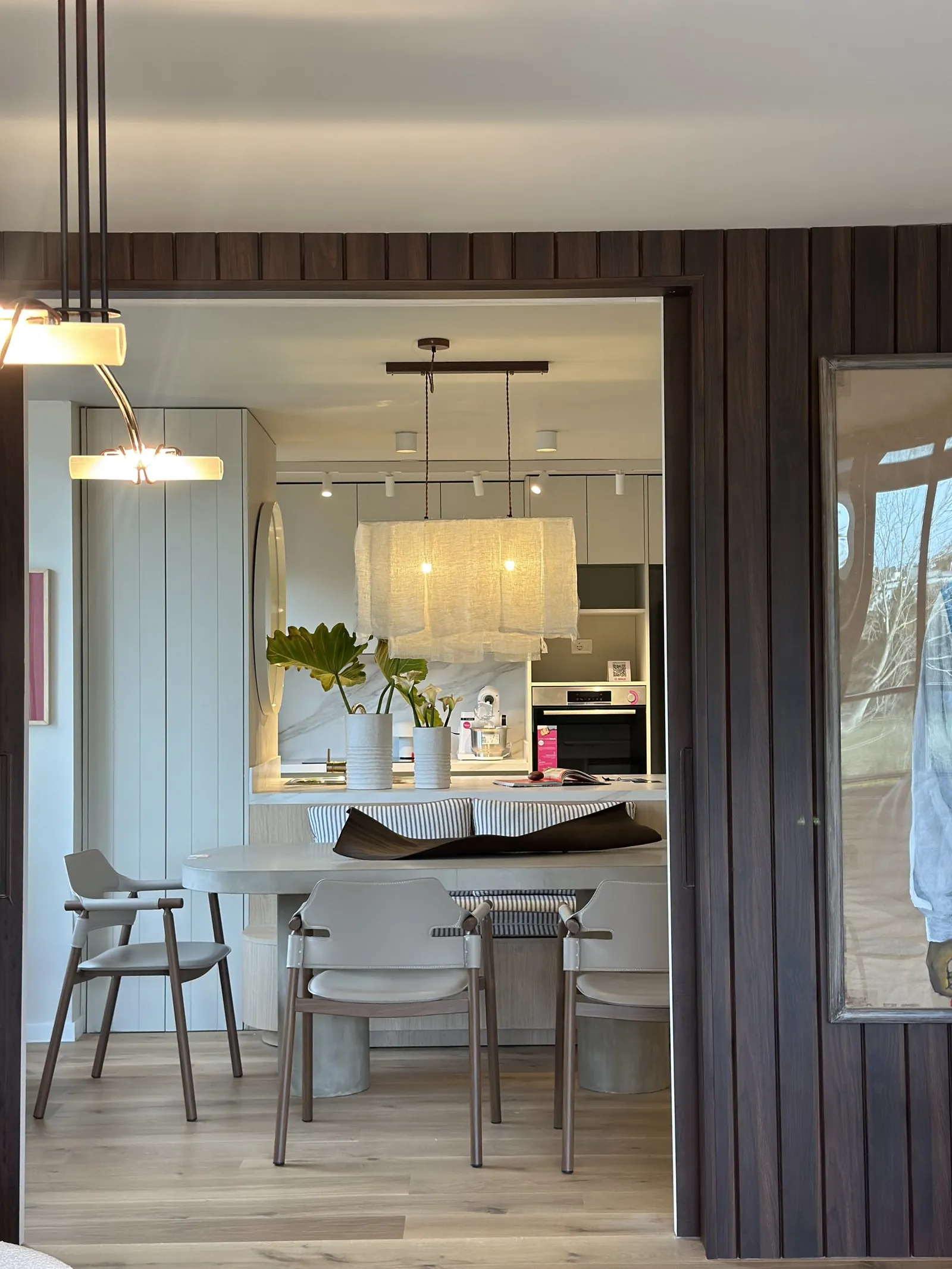 Comedor visto a través de un vano de madera, con mesa, sillas y la cocina al fondo