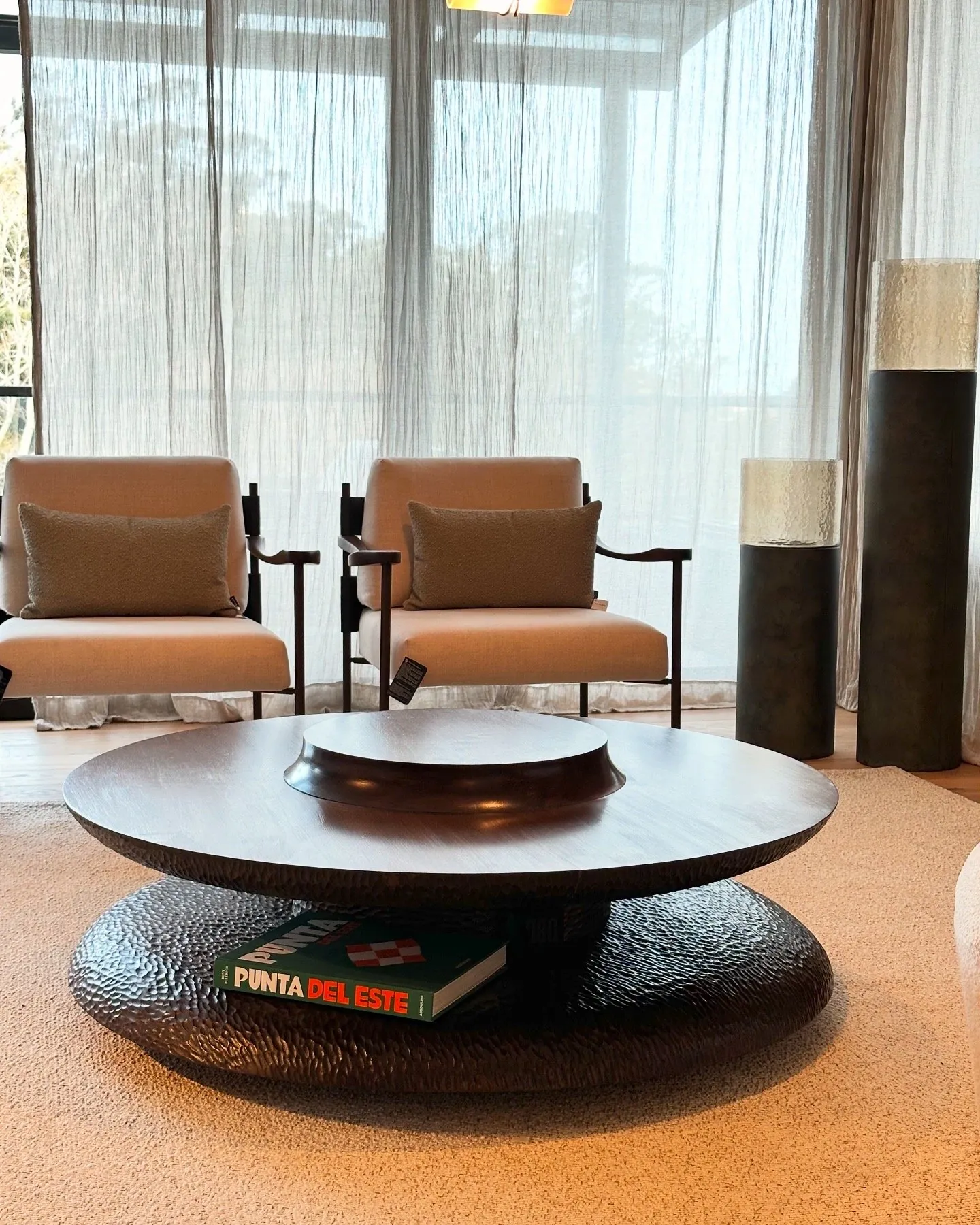 Estar con dos sillones claros y una mesa de centro redonda de madera