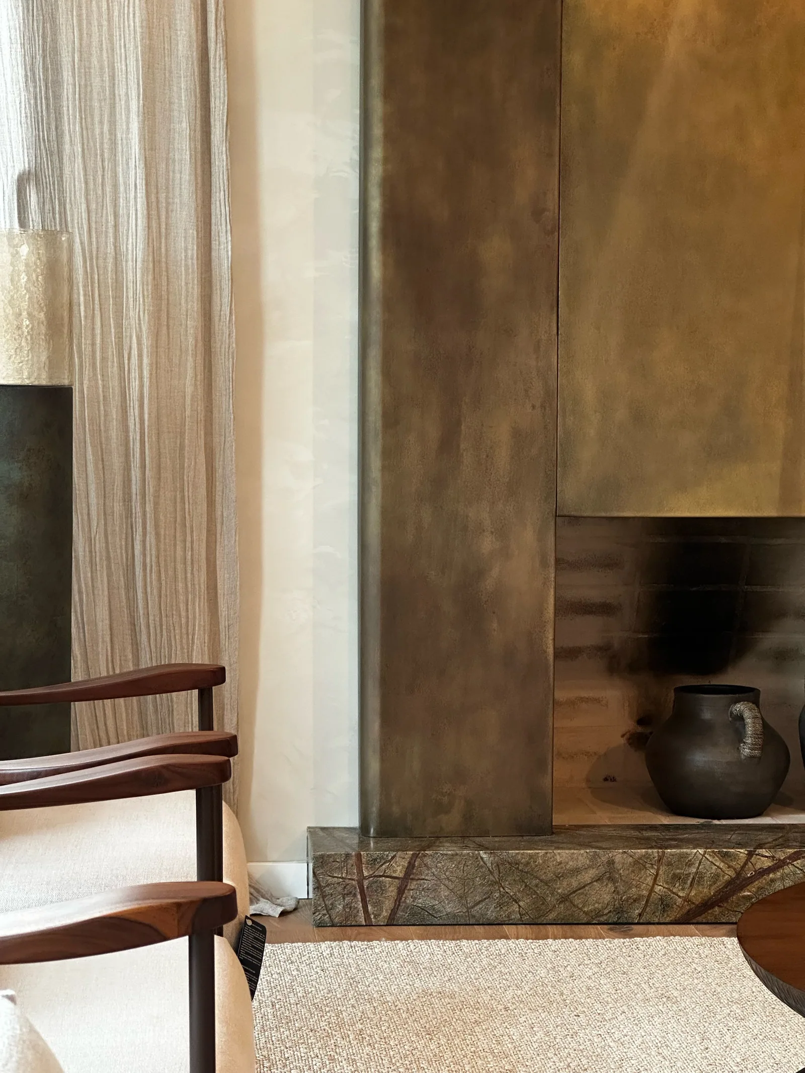 Chimenea de latón con dos vasijas, sillones claros y una mesa de madera