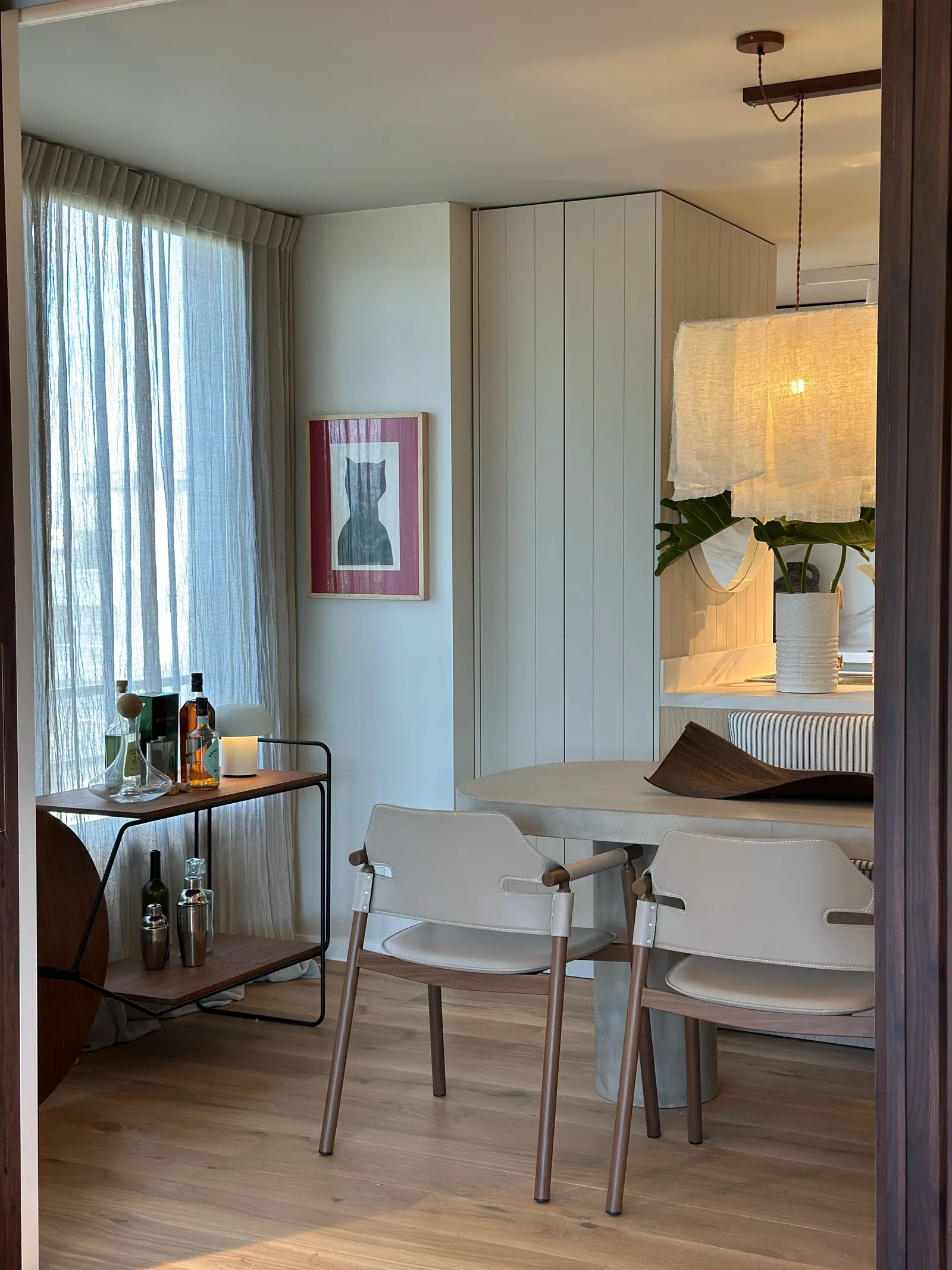 Comedor con mesa de madera, sillas claras, carrito de bar y lámpara colgante