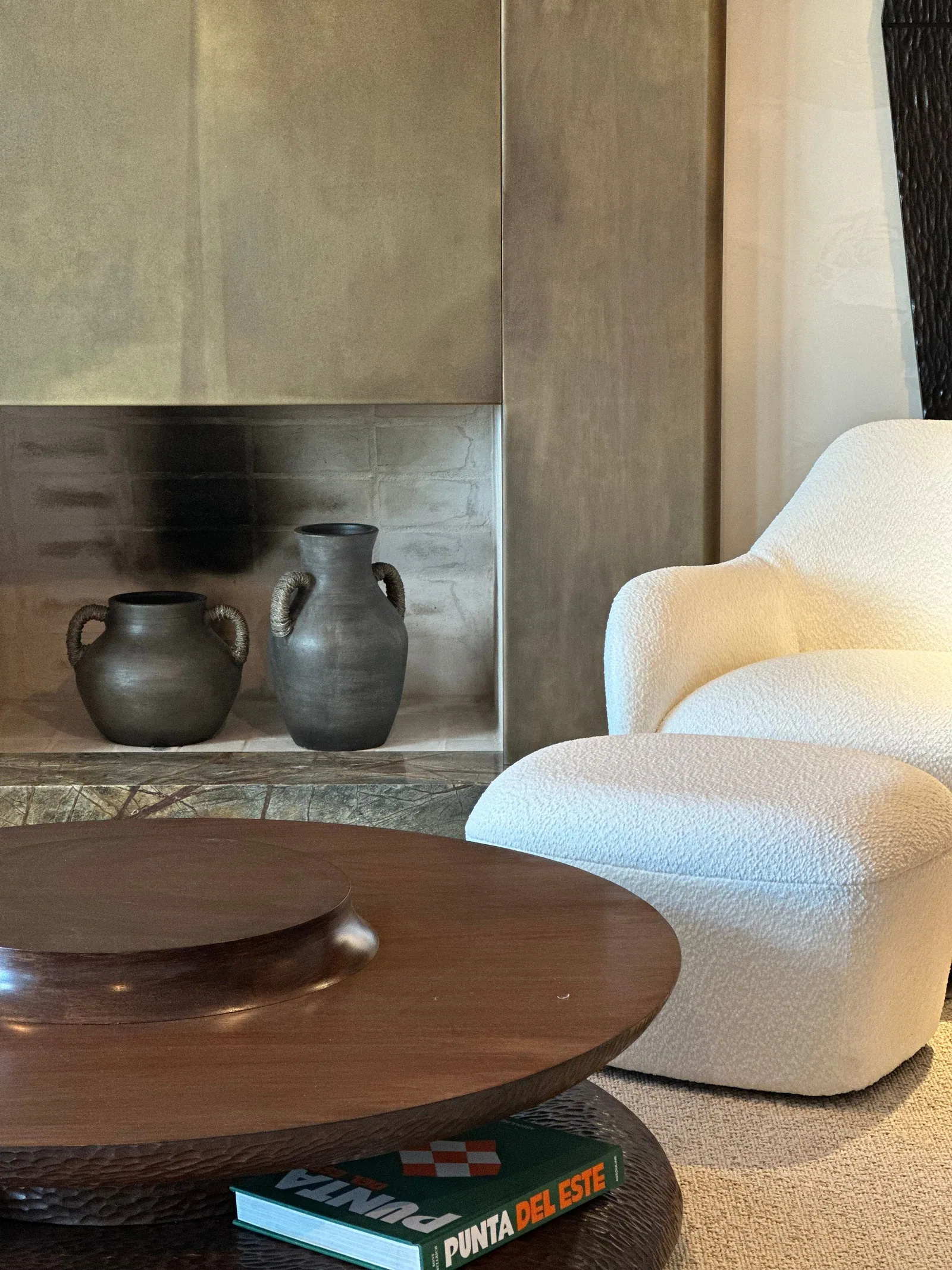 CDO | La mirada del coleccionista: chimenea de latón con dos vasijas de barro, sillón blanco de bouclé y mesa de madera redonda